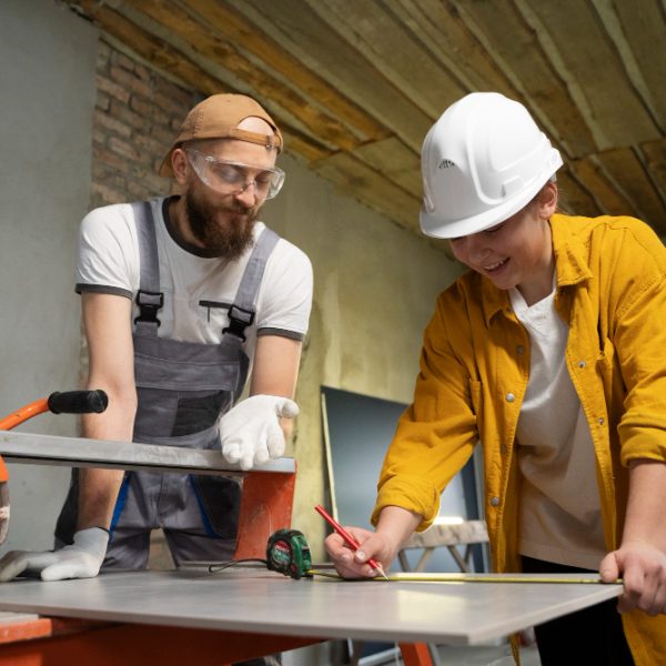 a man and woman in hardhats and hardhats measuring a piece of metal